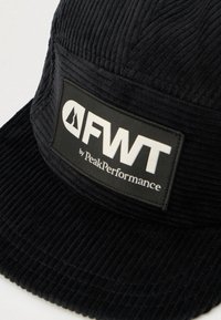 Zwarte pet van corduroy met een rechte klep, gestructureerde stof en een rechthoekige logopatch met de tekst "FWT by PeakPerformance."