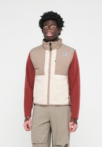 Lightweight, beige and cream fleece vest with high collar, front zipper, and red long sleeves. Notable branding on upper left chest.