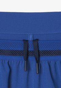 Pantaloni sportivi blu con cintura liscia, pannello in rete e cordino con estremità in plastica nera. La texture è morbida e leggera.