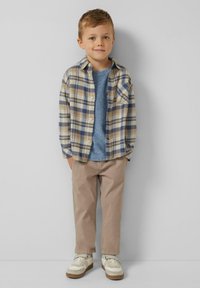 Koszula w kratę w odcieniach beżu, niebieskiego i kremowego, noszona na niebieskiej koszulce; beżowe spodnie i białe trampki z beżowymi akcentami. Dobrze pasuje do dziecka.