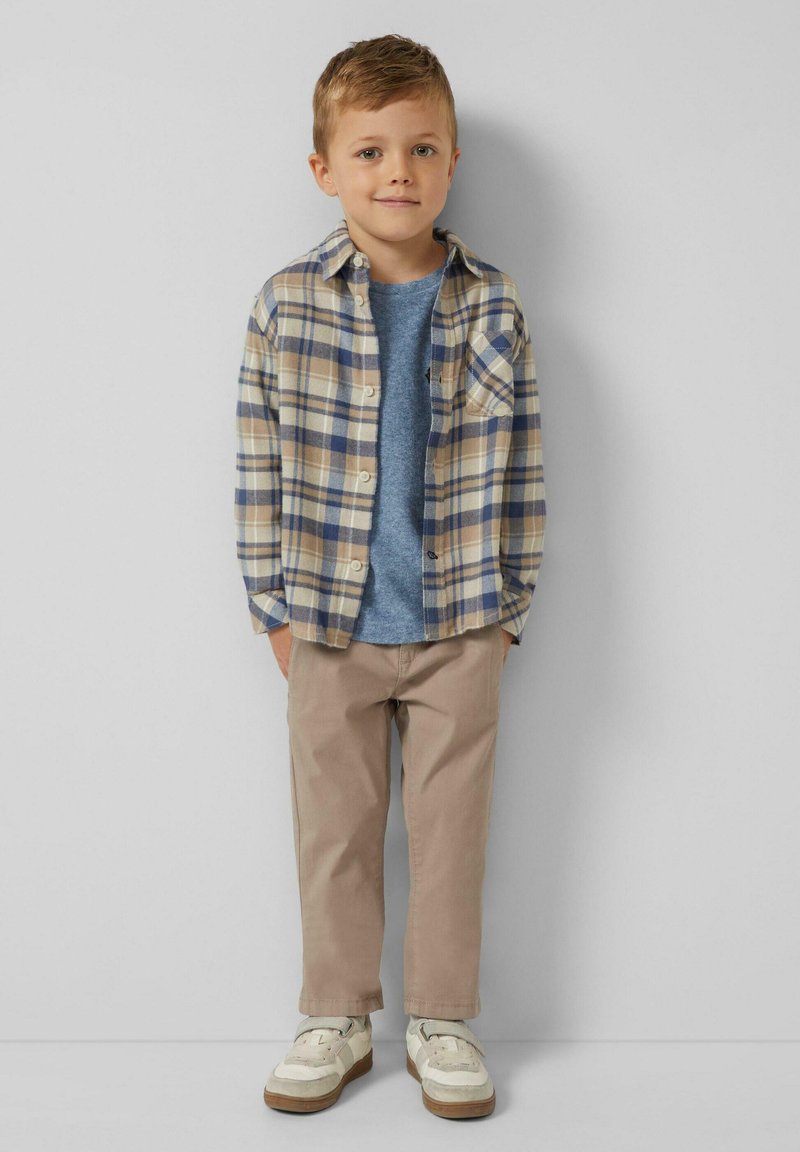 Koszula w kratę w odcieniach beżu, niebieskiego i kremowego, noszona na niebieskiej koszulce; beżowe spodnie i białe trampki z beżowymi akcentami. Dobrze pasuje do dziecka.