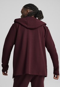 Felpa con cappuccio color bordeaux, maniche lunghe, texture morbida e vestibilità rilassata. Presenta un orlo curvo e dettagli di cucitura discreti.