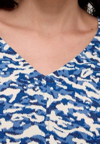 Tessuto blu e bianco con motivo a V, caratterizzato da una superficie testurizzata e forme astratte ondulate di diverse tonalità di blu.