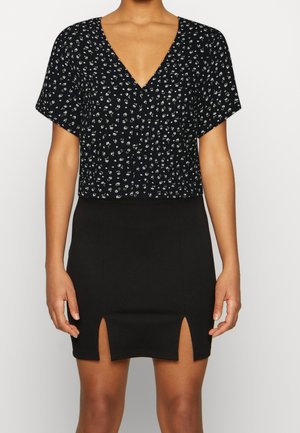 Schwarzes V-Ausschnitt-Crop-Top mit floralem Muster; kombiniert mit einem enganliegenden schwarzen Rock mit zwei seitlichen Schlitzen. Glatte Textur, lässiges Design.