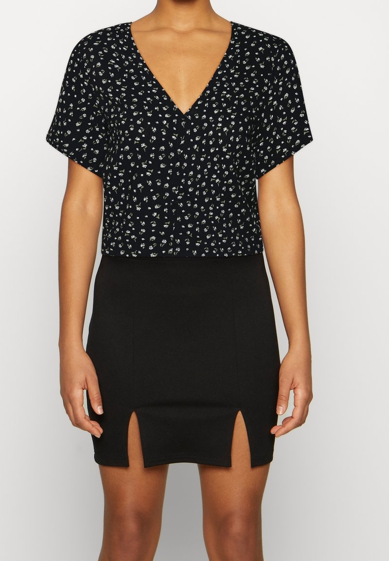 Black V-neck cropped top with a floral pattern; paired with a fitted black skirt featuring two side slits. Smooth texture, casual design.