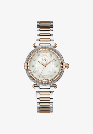 Srebrny i różowozłoty zegarek z okrągłą tarczą, tarczą z masy perłowej, diamentowymi akcentami oraz metalową bransoletą. Na tarczy umieszczono cyfry rzymskie XII i VI.