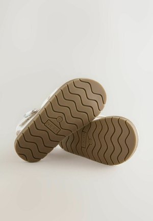 Sandalias transparentes con suela de goma y dibujo gruñido marrón. Cuentan con una correa ajustable y marca en la suela. Parte superior transparente.