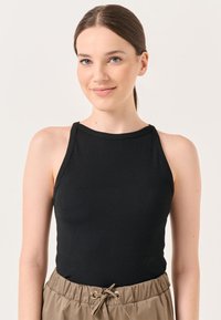 Schwarzes, geripptes Tanktop mit rundem Ausschnitt und dünnen Trägern, kombiniert mit beigen Jogginghosen mit einem gerafften Bund.