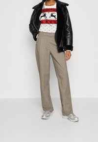 Czarna skórzana kurtka z futrzanym kołnierzem, biała sweter świąteczny z czerwonymi akcentami i beżowe teksturowane spodnie, w połączeniu z srebrnymi trampkami.