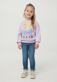 Felpa viola con design di cartone animato raffigurante una ragazza; con polsini e orlo a coste. Abbinata a jeans blu e sneaker bianche.