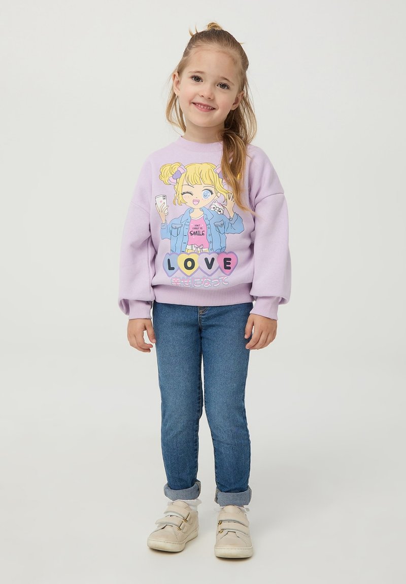 Felpa viola con design di cartone animato raffigurante una ragazza; con polsini e orlo a coste. Abbinata a jeans blu e sneaker bianche.