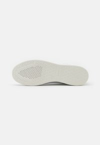 Suola di sneaker bianca con un motivo testurizzato, perforazioni circolari per la traspirabilità e un sottile design geometrico per la presa.