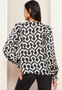 Blusa a righe bianco e nero con spalle arricciate, maniche lunghe e polsini elasticizzati. Tessuto morbido con un taglio fluido.