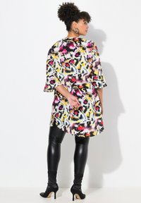 Bunt gemusterte Tunika mit floralem Design und ¾-Ärmeln in Glockenform, kombiniert mit schwarzen Leggings und knöchellangen, mit Absatz versehenen Stiefeln. Glatte Stofftextur.