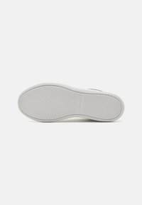 Fehér gumis sneaker talp, texturált tapadási mintával, a sarok közelében egy kis logóval, amely kiemelkedik. Simább élek és kerekded forma.