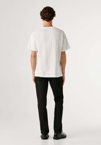 Camiseta blanca de manga corta con escote redondo y detalles de aberturas laterales, combinada con pantalones negros de corte ajustado y zapatos negros.