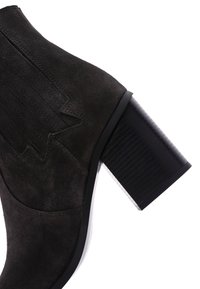 Bottine en suède noir avec un talon en bloc texturé, présentant des accents verticaux nervurés sur les côtés et un bout arrondi.