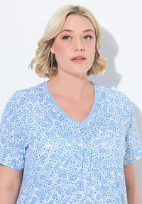 Top de manga corta azul claro con un patrón floral en varias tonalidades de azul y blanco, con escote en V y textura suave.