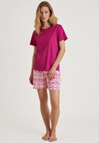 Frambozenroze t-shirt met korte mouwen, gecombineerd met witte shorts met een levendig roze en groene geometrisch patroon.