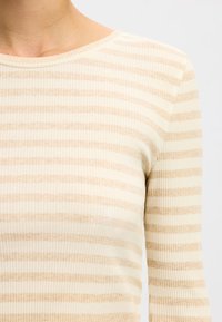 Dolga ropa z ribanim vzorcem v kremni barvi z svetlobezhnimi vodoravnimi črtami. Ima zaobljen izrez in mehak, teksturiran material.