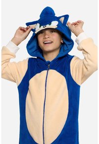 Niebieski polarowy kombinezon z beżowymi akcentami, z kapturem z uszami, suwakowym przodem i wzorem twarzy Sonic the Hedgehog. Miękka i wygodna tekstura.