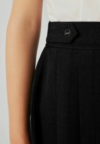 Pantaloni neri con vestibilità slim, realizzati in tessuto texturizzato, con pieghe nette e un distintivo bottone esagonale con dettaglio del logo.