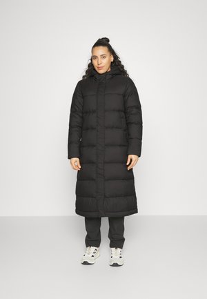 Black puffer coat with a hood, featuring quilted sections and a mid-calf length, paired with black pants and white sneakers.
