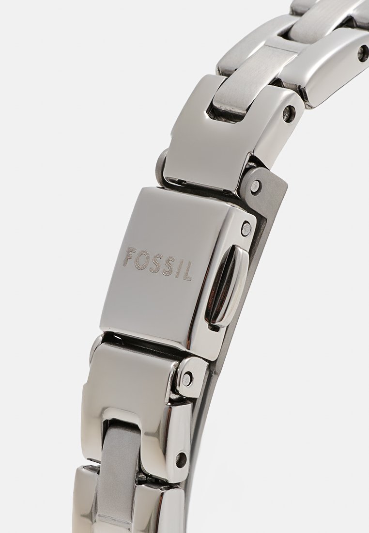 Bracelet de montre en métal poli argenté, avec des maillons rectangulaires, logo "FOSSIL" gravé sur le fermoir, et une texture lisse et élégante.