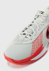 White athletic shoe with red accents, mesh upper, perforated details, and a textured sole. Features a visible Air Zoom logo.