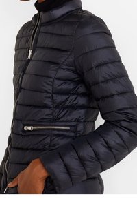 Czarna kurtka puchowa z pikowanym wzorem, wysokim kołnierzem i zipowanym kieszonką na piersi. Charakteryzuje się gładką, błyszczącą teksturą i dopasowanymi rękawami.