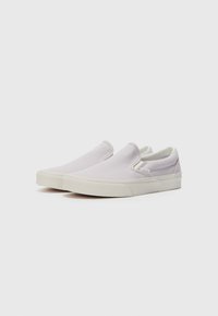 Sapatilhas em tela lilás claro, tipo slip-on, com detalhes elásticos nas laterais e solas de borracha brancas. Textura suave e design minimalista, sem atacadores.