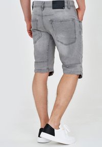 Shorts en jean gris avec une finition légèrement délavée, dotés de deux poches arrière et d'un ourlet retroussé. Taille ajustable avec un détail d'étiquette noire.