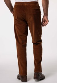 Pantalones de pana marrón con una superficie texturizada, cinturilla elástica y un solo bolsillo trasero. Las piernas se estrechan ligeramente en los puños.