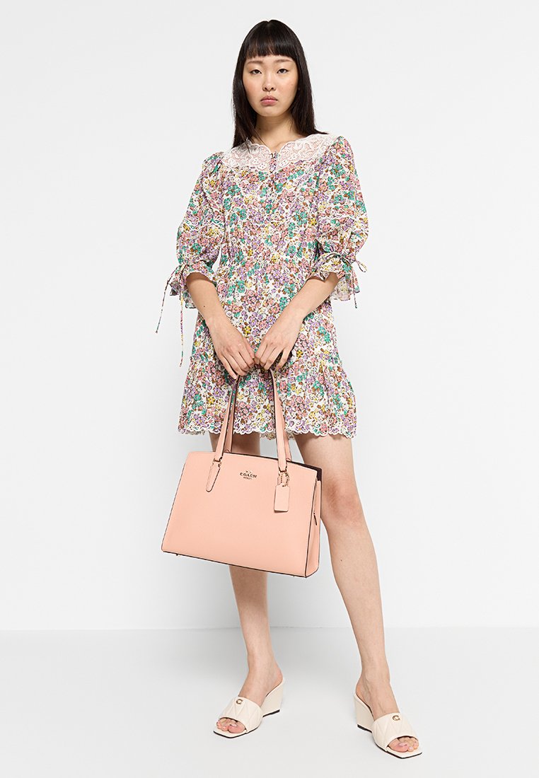 Blommig klänning med puffärmar och spetsdetaljer; ljusrosa läderhandväska med dubbla handtag och logotyp; beige slidessandaler.