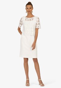 Weißes Kleid mit kurzen Spitzenärmel, rundem Halsausschnitt und einem glatten, taillierten Rock. Details umfassen ein florales Spitzenmuster und einen sauberen Saum.