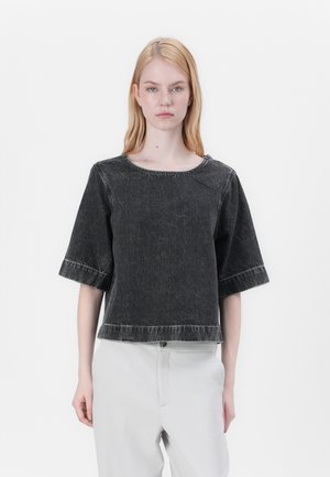Top corto in denim nero con ampiezza a maniche corte, caratterizzato da un collo rotondo e cuciture a contrasto. Abbinato a pantaloni chiari.