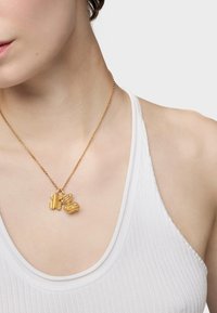 Złota naszyjnik z dwoma zawieszkami: jedna ma kształt misia w paski, a druga posiada teksturowany, kulisty wzór, zawieszona na cienkim łańcuszku.