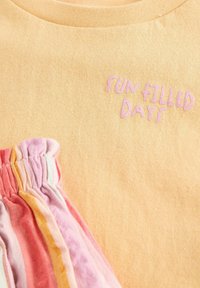 Geel katoenen T-shirt met de tekst "SUN FILLED DAYS" in roze borduursel, gecombineerd met meerkleurige gestreepte stofruffels.