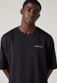 T-shirt preta de algodão com mangas curtas e decote redondo. Logótipo bordado "LEVI STRAUSS & CO." em dourado no lado esquerdo do peito.