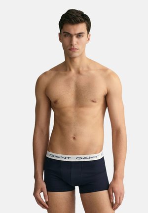 Boxer de color azul marino con una cinturilla elástica que presenta texto de logo en blanco. Tejido suave, diseño ajustado y longitud hasta la mitad del muslo.