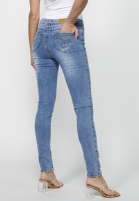 Skinny blue denim jeans with a mid-rise fit, featuring back pockets with stitching details, and light distressing along the legs.