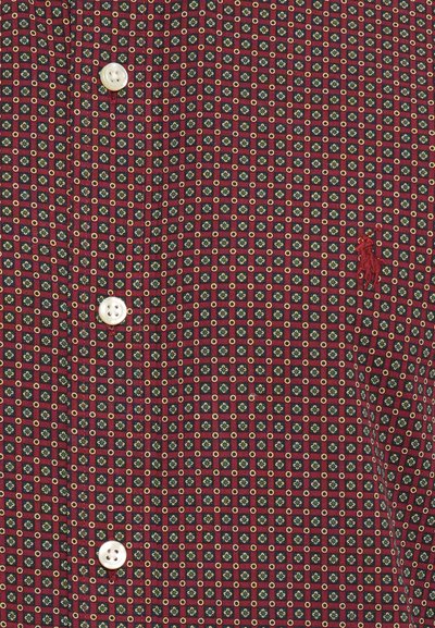 Cămașă cu nasturi, dintr-un material cu un model roșu și bleumarin, prezentând mici desene geometrice galbene și verzi, accentuată de nasturi albi și o broderie cu logo.