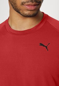 Rotes Sport-T-Shirt aus glattem Material, mit kurzen Ärmeln und einem schwarzen Puma-Logo auf der linken Brustseite.