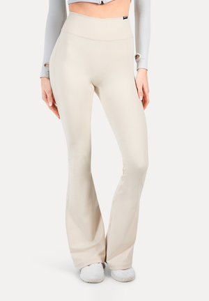 Beige hoge taille flared leggings gemaakt van een rekstof, met een gladde textuur en een minimalistisch ontwerp, gecombineerd met witte sneakers.