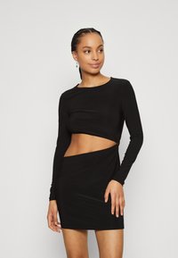 Robe noire à manches longues avec un haut court et un détail torsadé à la taille. Texture lisse, design ajusté, longueur mini et encolure ras du cou.