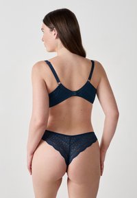 Set di reggiseno e perizoma in pizzo blu navy con motivi geometrici, spalline regolabili e bordi ondulati, che mettono in mostra dettagli di texture intricati.