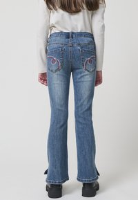 Jeans acampanados de lavado claro, con bolsillos traseros bordados con un patrón en espiral y un ligero deshilachado en el dobladillo.