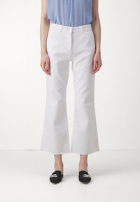 Jean flare blanc avec un ourlet effiloché, en tissu denim, associé à des chaussures noires à enfiler avec des accents décoratifs.