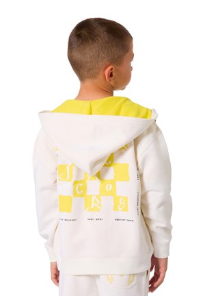 Sweat à capuche blanc avec un bord jaune et un imprimé graphique au dos. Le design présente des formes géométriques et des éléments textuels ludiques.
