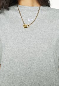 Szara bawełniana koszulka z małym białym logo Nike na piersi, w połączeniu z złotym łańcuchem z zawieszką w kształcie kłódki.